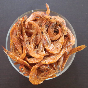 Dried shrimp in a bowl on a wooden surface, showing their orange color and curled shapes