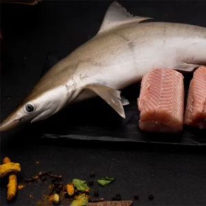 Whole raw fish and cut fish fillets placed on a black surface with scattered spices and herbs baby shark