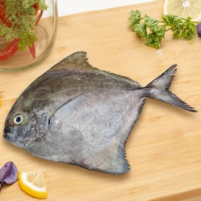 Fresh pomfret fish placed on a wooden cutting board with lemon slices and herbs nearby
