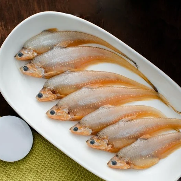 Golden anchovy fish neatly arranged on a white plate, showing their slender bodies and light orange-silver color